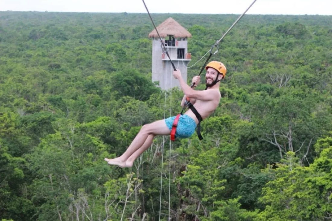 Smiling man ziplining above the jungle canopy