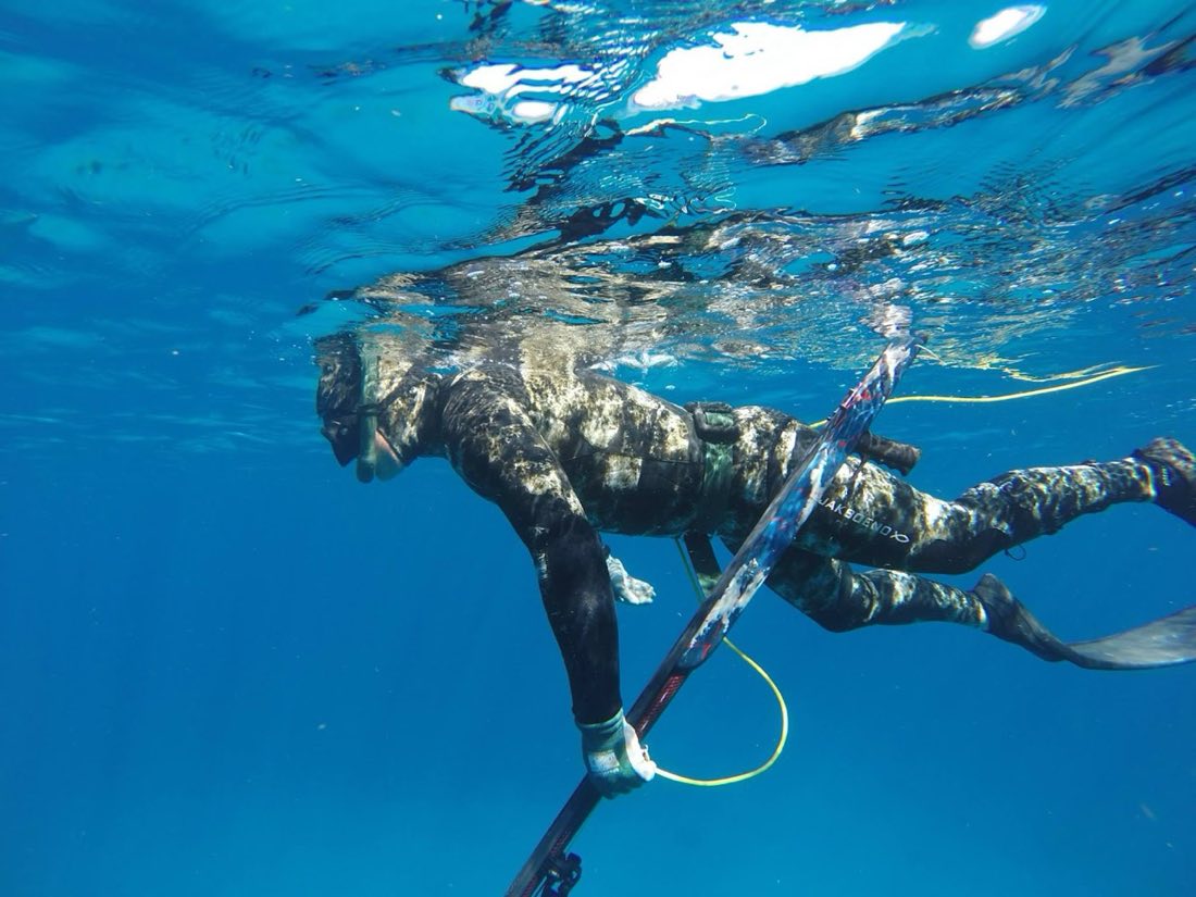 Freediver with speargun beneath the turquoise sea surface