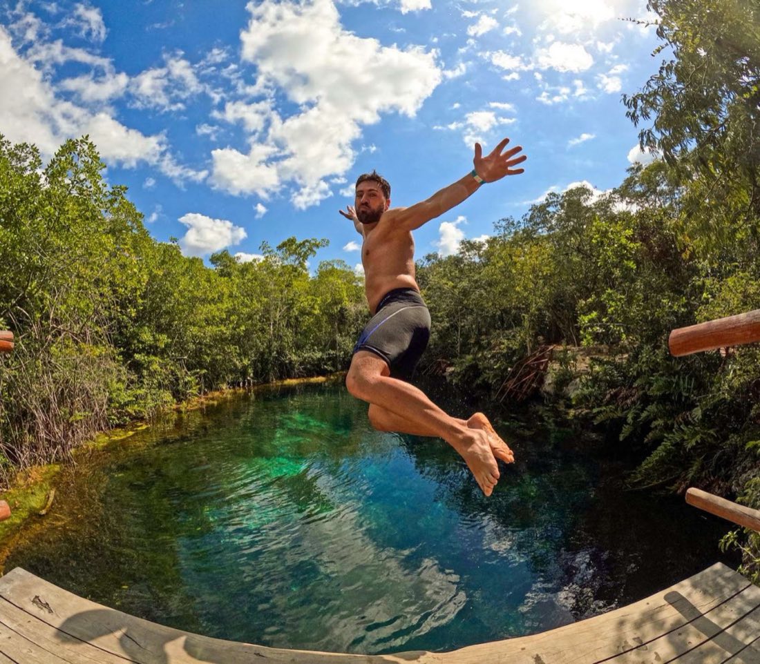 Man leaping into a turquoise cenote from a wooden deck